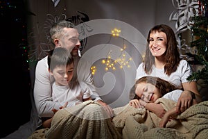 Lovely Family with mother, father, son and daughter having fun in room derorated fot Christmas night. Children and