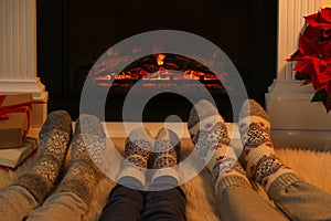 Lovely family in warm socks resting near fireplace at home, closeup