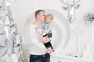 Lovely father keeping son on hands, hugging and kissing him in christmas studio