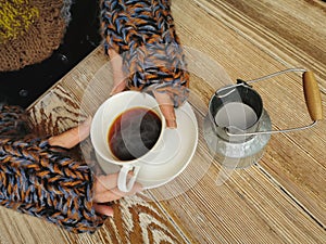 Lovely female hands holding a white Cup of hot coffee. A girl in a Cozy warm knitted sweater holding a Cup of hot coffee