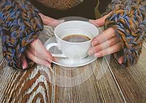 Lovely female hands holding a white Cup of hot coffee. A girl in a Cozy warm knitted sweater holding a Cup of hot coffee