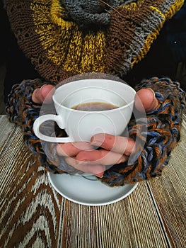 Lovely female hands holding a white Cup of hot coffee. A girl in a Cozy warm knitted sweater holding a Cup of hot coffee