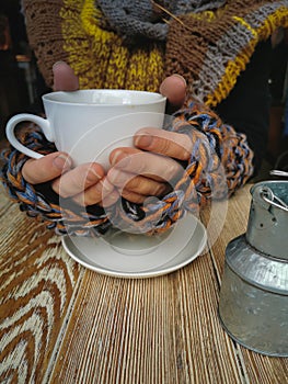 Lovely female hands holding a white Cup of hot coffee. A girl in a Cozy warm knitted sweater holding a Cup of hot coffee