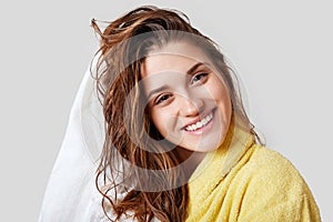 Lovely female with wet hair, takes shower, dries head with towel, being pleased after taking bath, dressed in yellow bathrobe, pos