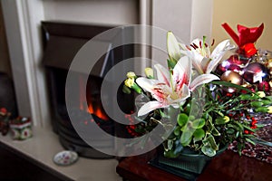 Lovely festive Christmas flower arrangement with lilies and carnations, fireplace in background, copy space for text