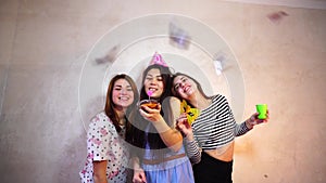 Lovely friendly girls celebrate birthday of their female friends and have fun standing on background of light wall in