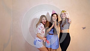 Lovely friendly girls celebrate birthday of their female friends and have fun standing on background of light wall in