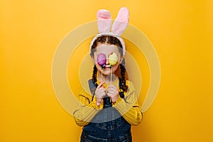 Lovely funny sweet preschool girl kid hiding eyes behind colored eggs on sticks, dressed in pink bunny fluffy ears