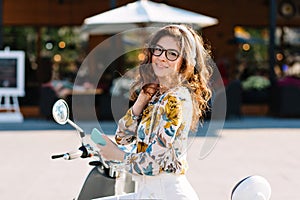 Lovely girl with beautiful dark-brown hair looking with interest while waiting friend in front of cafe. Portrait of good