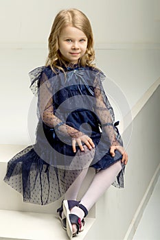 Lovely girl in blue dress sitting on white ladder