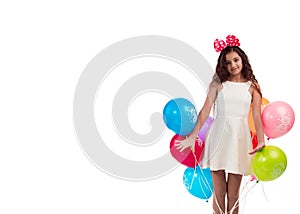 Lovely girl brunette with long hair in a white dress with a bow on her head and balloons posing on a white background