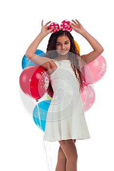 Lovely girl brunette with long hair in a white dress with a bow on her head and balloons posing on a white background