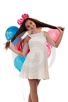 Lovely girl brunette with long hair in a white dress with a bow on her head and balloons posing on a white background