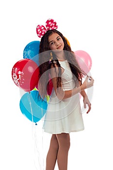 Lovely girl brunette with long hair in a white dress with a bow on her head and balloons posing on a white background