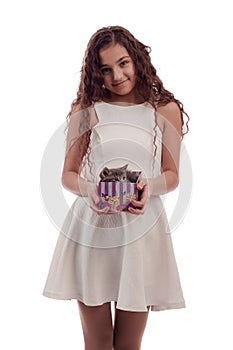 Lovely girl brunette with long hair in a white dress with a small gray kitten in a gift box in his hands on a white background in