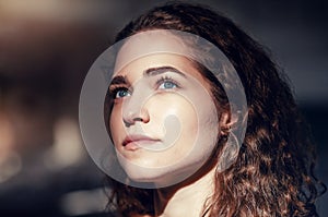 Lovely girl close-up portrait, face lit by ray of sunshine, contrasting photo