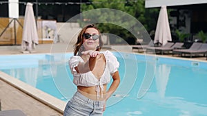 Lovely girl model posing and smiling at swimming pool in skirt, blouse and sunglasses at luxury outdoor club. Attractive