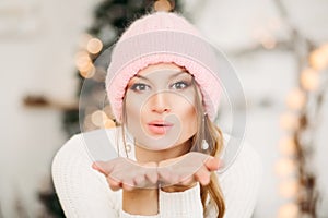 Lovely girl in pink woolen beanie hat making air kiss with hands.