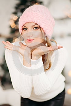 Lovely girl in pink woolen beanie hat making air kiss with hands.