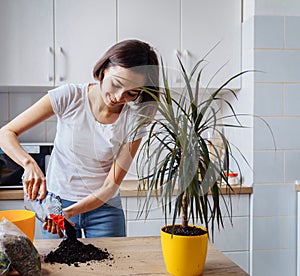 Lovely girl replanting flowers at home  relaxing after working day. Pouring the ground and fertilizer from the packaging  mixing