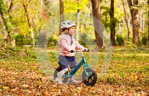 Lovely girl riding balance bike in atumn park