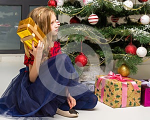 Lovely Girl Sitting on Floor in Front of Christmas Tree with Gift Box.