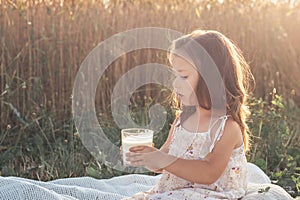 Lovely girl in is sitting on summer day in field against background of cereals with glass ofmilk.