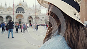 Lovely girl in straw hat walks on San Marco square, looks back and cute smiles