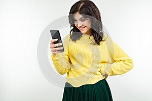 Lovely girl in a yellow blouse smilingly peeks at a message on the phone on a white background photo