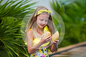 Lovely girl in yellow swimsuit holds yellow mango on vacation in the tropics