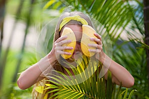 Lovely girl in yellow swimsuit holds a yellow mango on vacation in the tropics