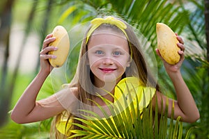 Lovely girl in yellow swimsuit holds a yellow mango on vacation in the tropics