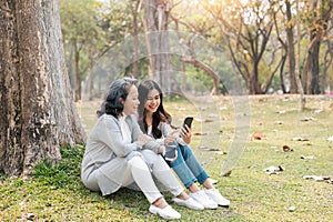 Lovely granddaughter and grandmother sitting under the tree in the green park together, watching Social news on