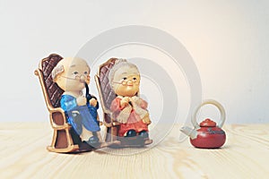 Lovely grandparent doll siting old sofa classic chair together on wooden table with background.