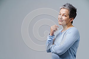 Lovely grey hair mature business woman in 50s posing sideways with hands folded and copy space on right isolated on