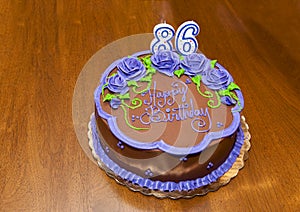 Lovely Happy 86th birthday cake with chocolate icing and purple flowers and number candles.
