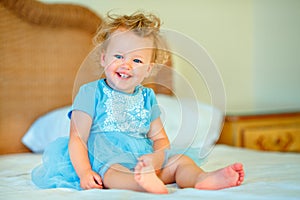 Lovely happy blonde toddler girl sitting on a bed