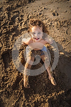 lovely happy child sitting on the sand looking up smiling