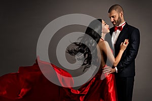 Lovely Happy Couple dancing. Woman in red Dress and Man in Black Suit with Bow Tie. Flying silk Fabric and hair on Wind. Studio
