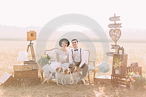 The lovely horizontal portrait of the vintage dressed newlyweds sitting with the dogs on the sofa surrounded with the