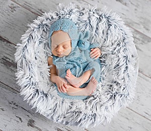 Lovely infant in hat and jumpsuit sleeping on round bed