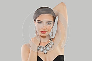 Lovely jewelry model woman with dark brown hair and shiny fresh skin wearing diamond earring and necklace posing against grey