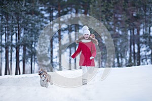 Lovely joyful girl running with a dog in the winter forest