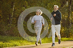 Lovely joyful retirees couple doing sports and jogging together in city park.