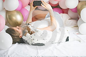 Lovely lady in pajama making selfie in her bedroom using phone and hanging out with her dog. Indoor portrait  girl with baloons in