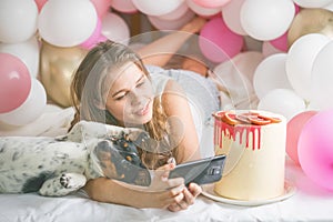 Lovely lady in pajama making selfie in her bedroom using phone and play with her dog. Indoor portrait  girl with baloons in