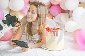 Lovely lady in pajama making selfie in her bedroom using phone and play with her dog. Indoor portrait  girl with baloons in