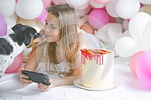 Lovely lady in pajama making selfie in her bedroom using phone and play with her dog. Indoor portrait  girl with baloons in