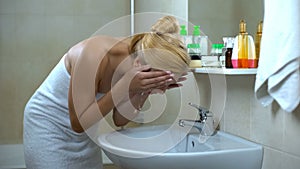 Lovely lady washing face in front of mirror, satisfied after cosmetician visit