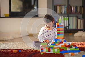 Lovely laughing little child, brunette girl of preschool age playing with colorful blocks sitting on a floor